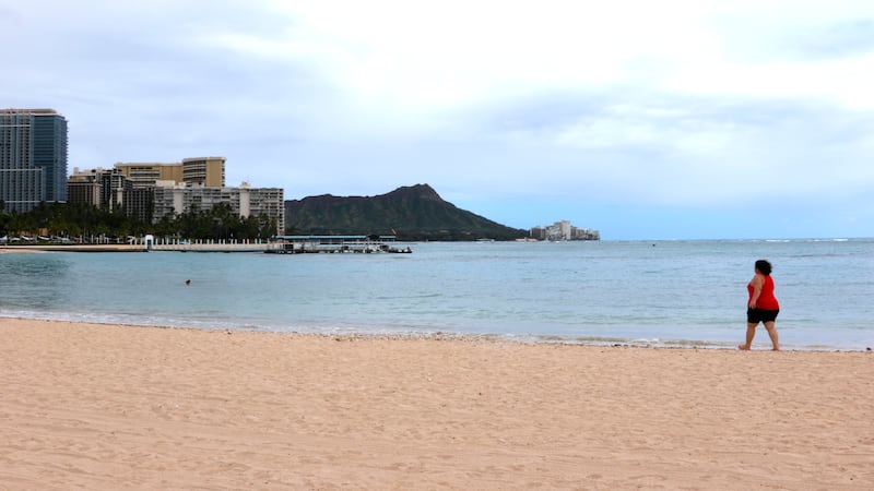 In this April 21, 2020, photo, a woman walks on Waikiki Beach in Honolulu.