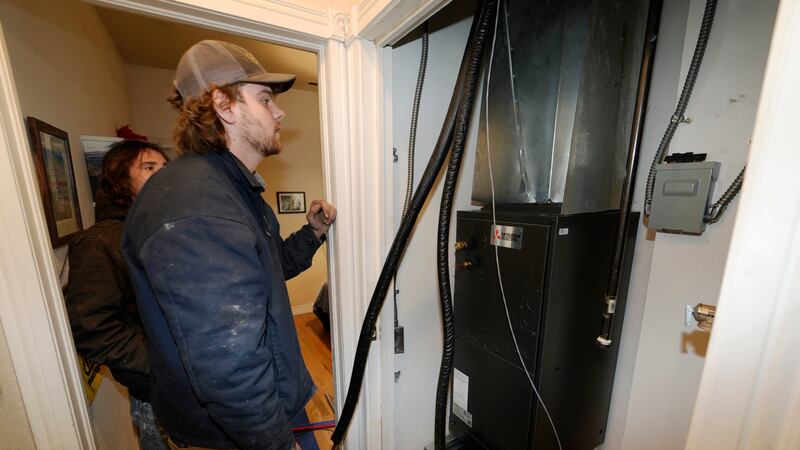 John Paul, front, and David Valenzuela work to install a heat pump in an 80-year-old rowhouse...